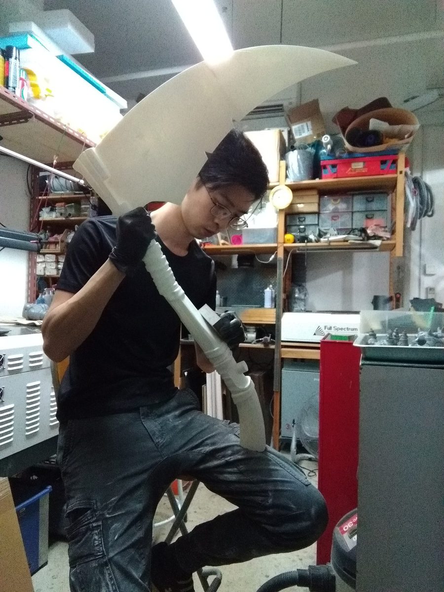 A Legion maker holding a large hand-fabricated scythe prop in the workshop