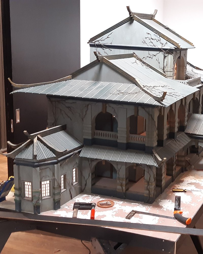 A large weathered scale model of a colonial mansion with interior lighting, on the workbench