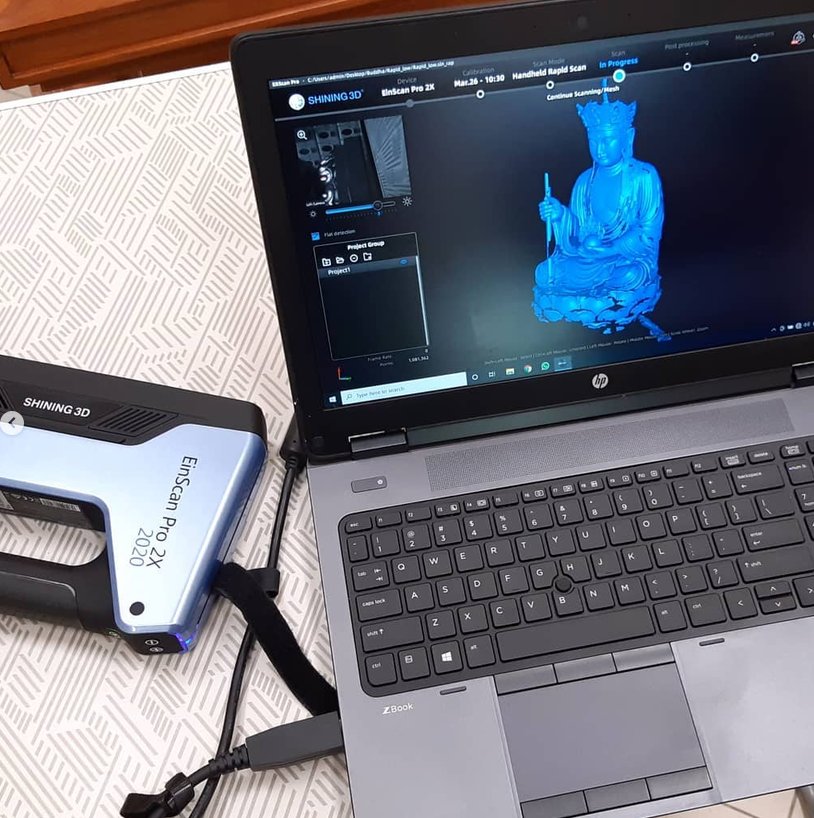 Handheld 3D scanner beside a laptop showing the live mesh capture of a statue